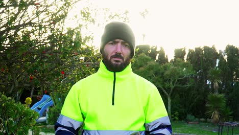 man with a beard and dressed in yellow reflective clothing, or a public worker uniform, with a hammer in his hand looking at the camera