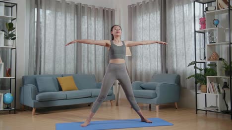 vista completa de joven entrenadora asiática mujer en ropa deportiva hablando y estirándose mientras enseña ejercicios en casa