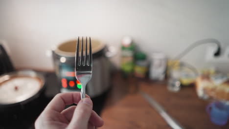 hand-held pov of a person holding a fork approaching a kitchen table with a multi-cooker flashing lights in the background