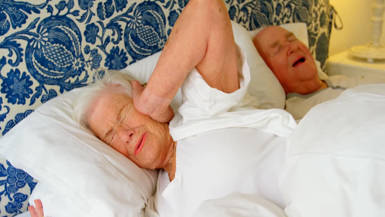 Caucasian senior woman getting disturbed with man snoring on bed at comfortable home 4k