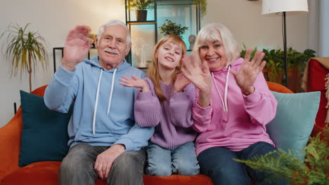 child girl granddaughter with grandparents waves hand hello hi relaxing making vlog on home sofa