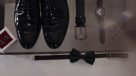 wedding grooms bow tie, cufflinks, clock and shoes lie on glass table