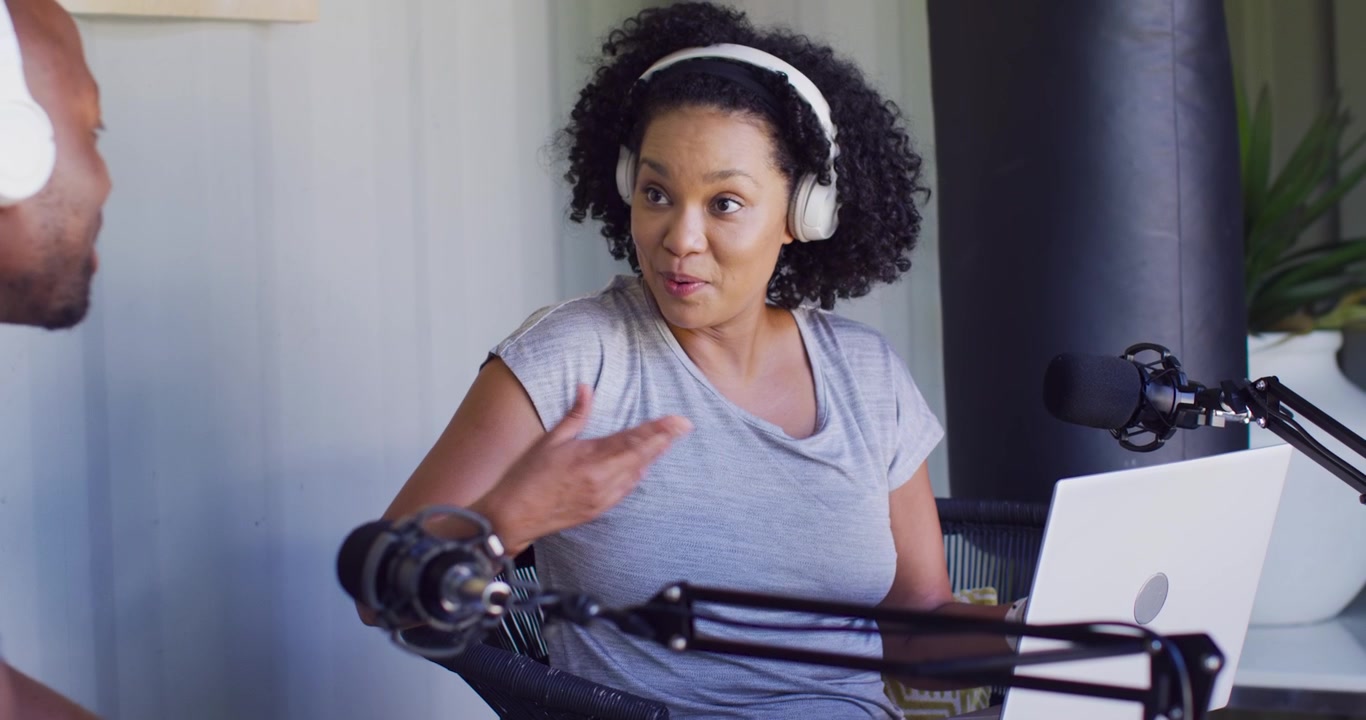 African American cohosts recording podcast home studio, woman reacting to man entering, mic, laptop