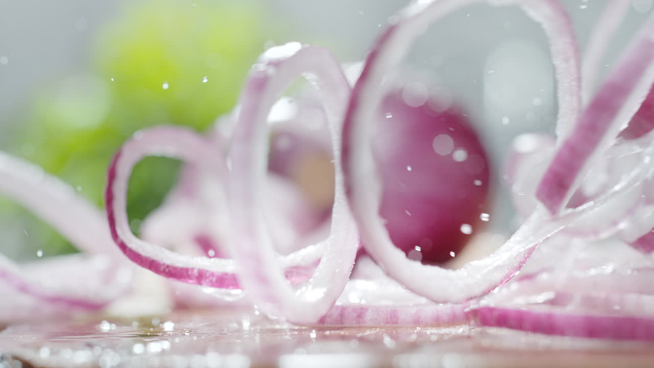 Red Onion Rings Fall Onto A Kitchen Counter, Roll, Bounce And Splash Water Droplets in Macro and Slow Motion