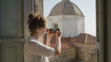 Mujer-Feliz-Usando-Un-Teléfono-Inteligente-Tomando-Fotos-Disfrutando-Compartiendo-La-Experiencia-De-Viaje-De-Vacaciones-De-Verano-Fotografiando-Hermosas-Vistas-Panorámicas-En-El-Balcón-Con-Gafas-De-Sol