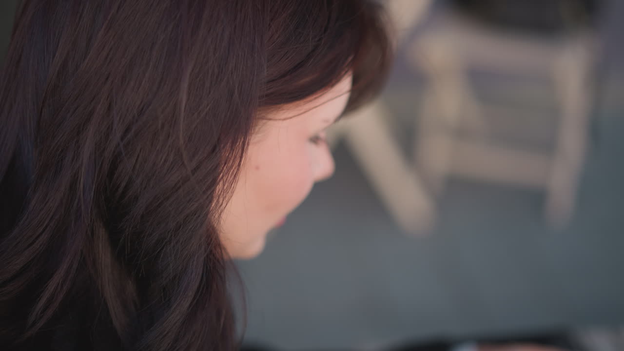 갈색 머리카락을 가진 여성의 클로즈업, 깊이 집중, 부드러운 표정, 의자를 보여주는 흐릿한 배경과 부드러운 야외 분위기를 가진 앉아