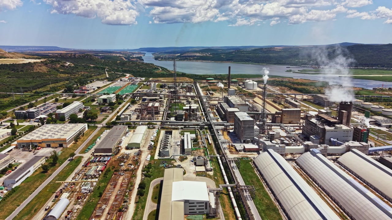 View of industrial area along the river with factories, machinery, and storage buildings during daytime with clouds in the sky