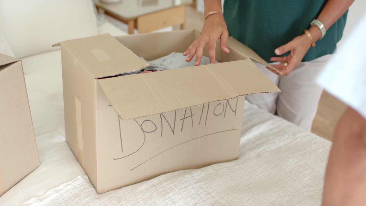African American couple, woman smiling holding shirt, packing DONATION box in bedroom for donation