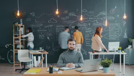 time lapse portrait of man sitting at desk in open space office while people colleagues working