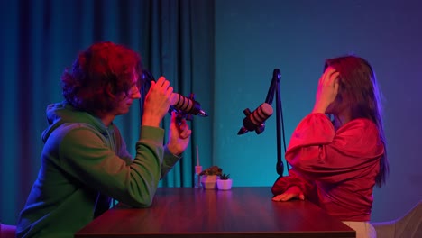 two people recording a podcast in a studio with colorful neon lighting