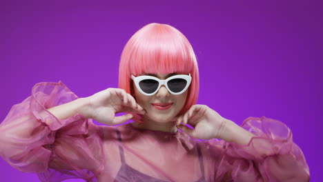 woman wearing a pink wig and fancy sunglasses while she dances and laughs to the camera