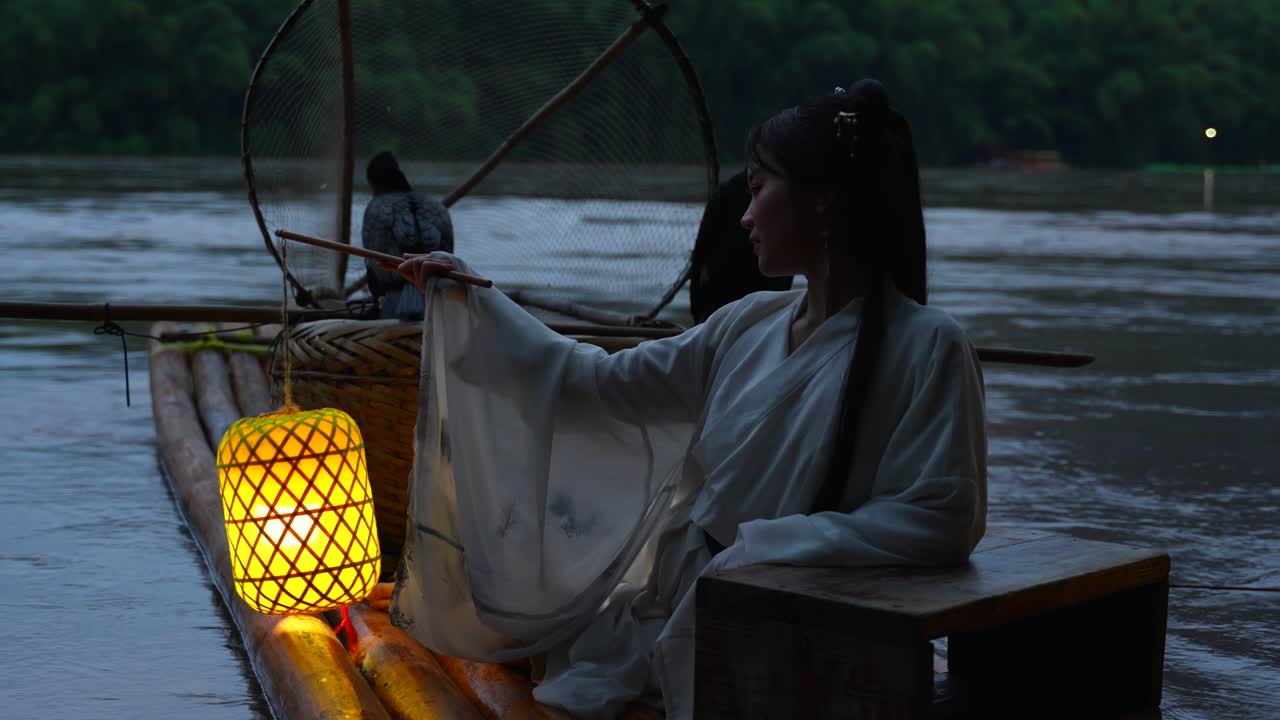 niña hanfu sosteniendo una linterna iluminada en una balsa de bambú con pájaros cormoranes por la noche