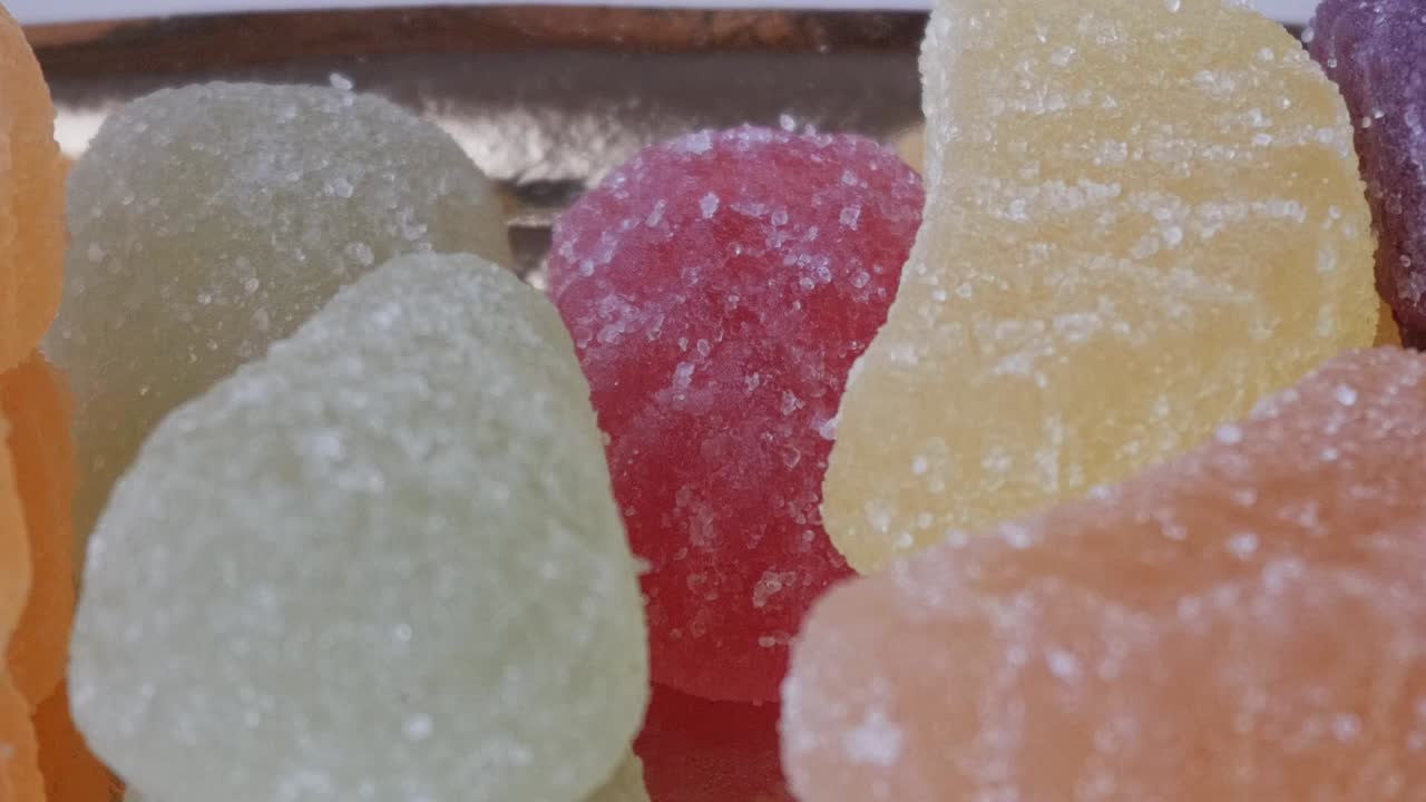 Detailed pan right of assorted sugar-coated jelly candies on a golden tray, with vibrant colors and sparkling sugar