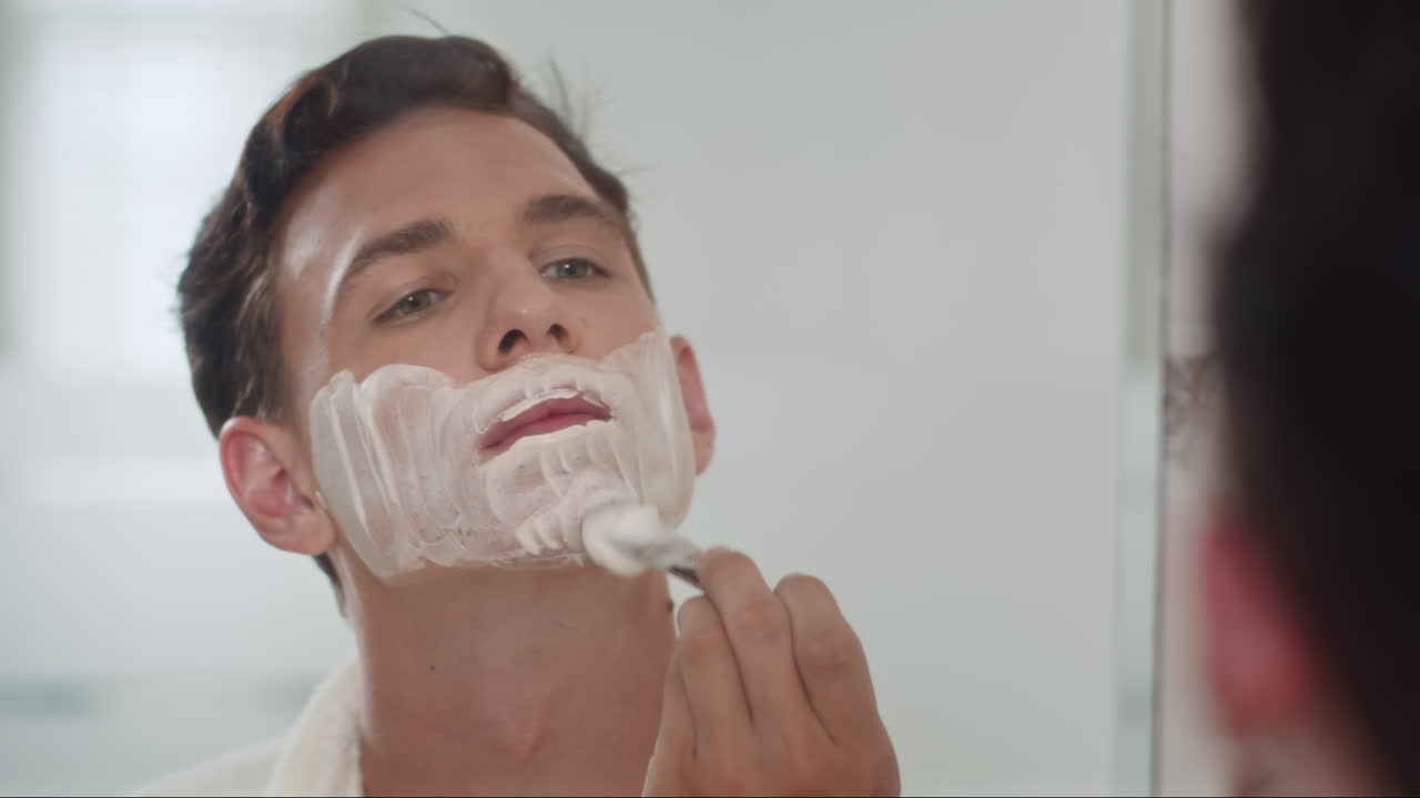 Guy with Brush and Bowl Applying Shaving Cream on Face in front of Mirror