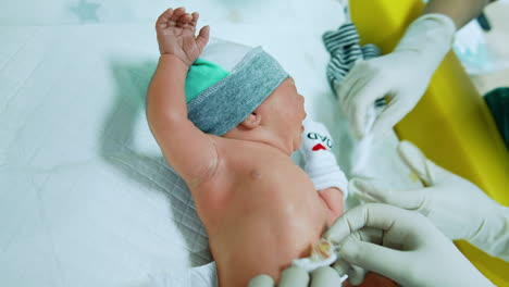 lovely newborn baby being dressed. child lies on the table while nurse in gloves puts mittens on tiny hands and other nurse takes care of navel.