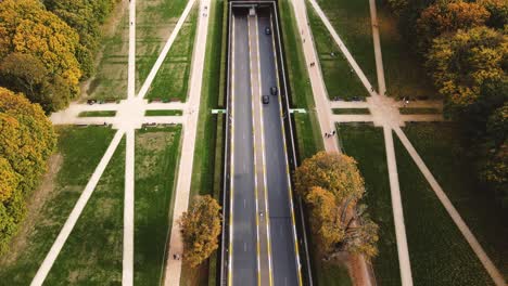 Aerial-View-of-two-cars-driving-on-a-road-going-under-the-Cinquantenaire-in-Brussels,-Belgium-tracking-shot-wide