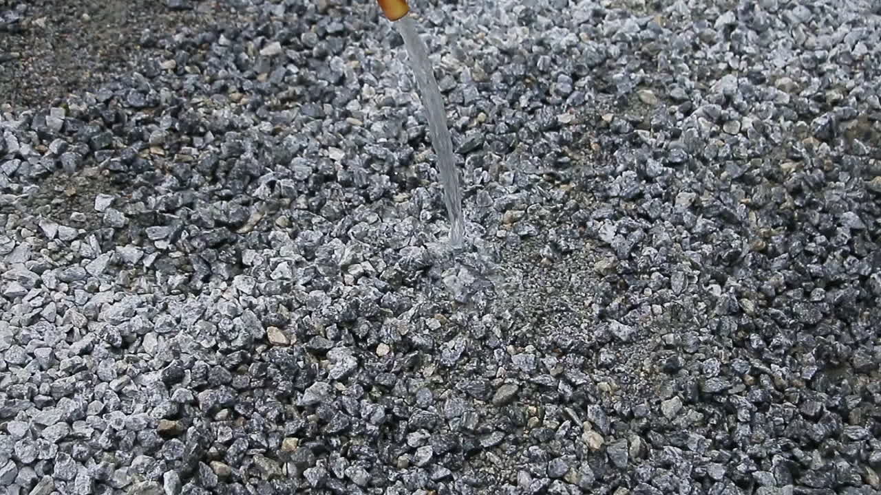 Indian mason worker pouring water over a gravel mix in preparation for mixing or setting the material
