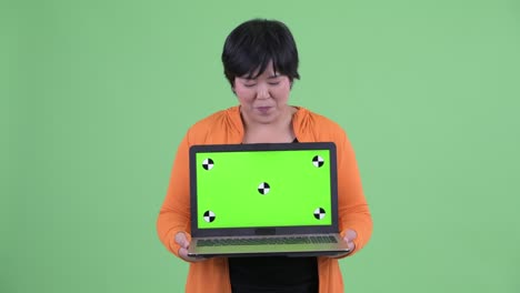 Studio shot of Asian woman smiling and showing laptop with copy space against green background