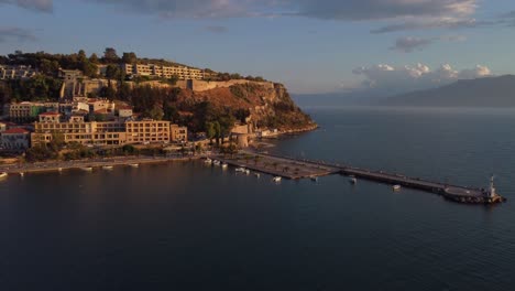 Aerial-view-of-the-small-Mediterranean-town-of-Nauplio-in-the-Peloponnese-region-of-Greece,-during-a-cloudy-afternoon-with-a-lighthouse-on-the-right-side-|-4K