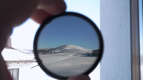 view of the snow-covered mountain peak through round tinted glass. the person holding camera 
nd filter and checking its opacity