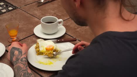 close-up shot over the shoulder of a tattooed person eating a homemade breakfast with eggs and coffee. great for food, culture, or lifestyle content.