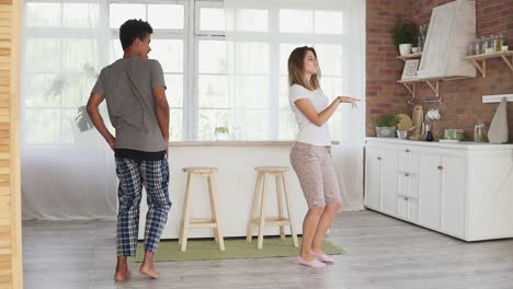 feliz pareja multirracial bailando en la cocina con pijama escuchando música por la mañana en casa. disparo en cámara lenta