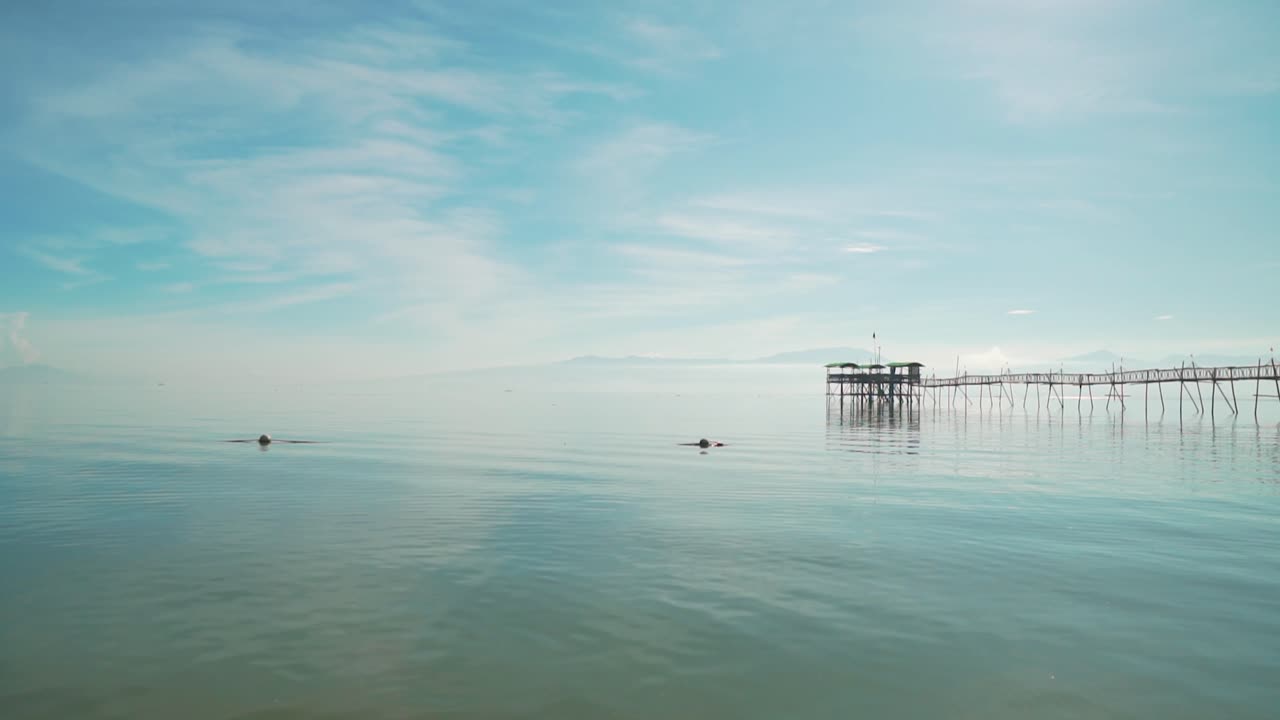 필리핀의 목조 부두 옆에 반사된 푸른 하늘과 구름이 있는 잔잔한 바다 파도