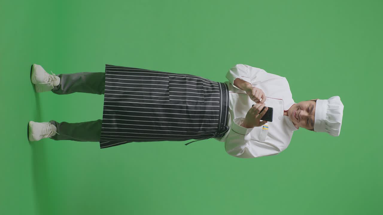 Full Body Of Asian Man Chef Looking At Smartphone Then Screaming Goal Celebrating While Standing In The Green Screen Background Studio