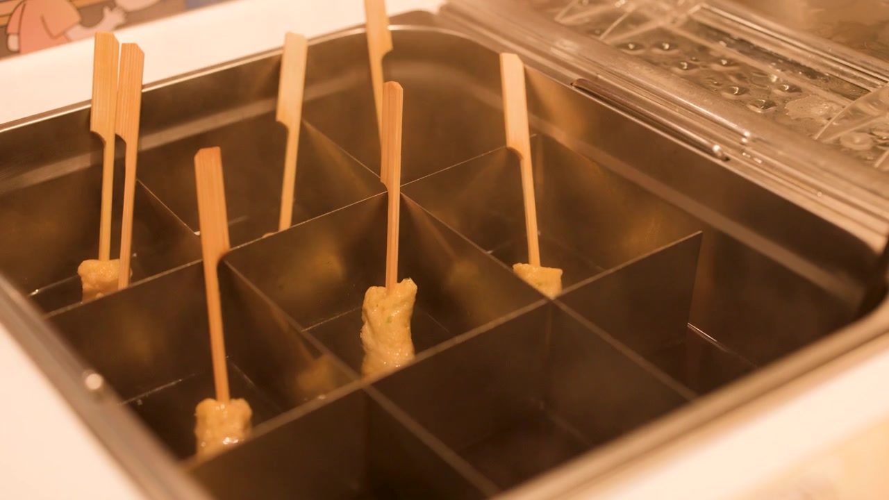 Tusuk sate odeng dimasak dalam kukusan logam bersekat dengan uap mengepul dan pencahayaan hangat