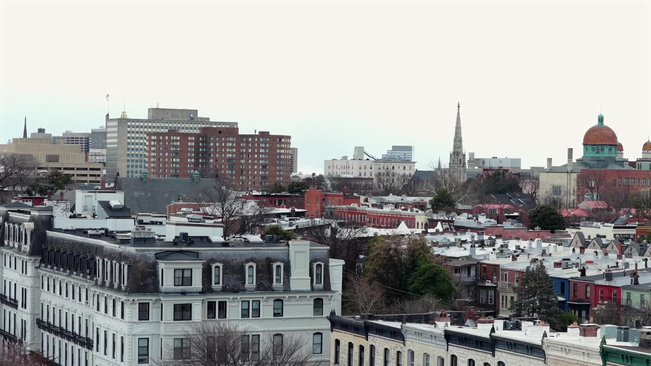 Quartiere Bolton Hill di Baltimora con case a schiera storiche, guglie di chiese e appartamenti di lusso di media altezza con lo skyline del centro che si staglia sullo sfondo. Ampia ripresa aerea.
