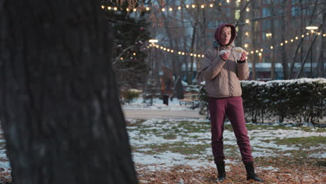 white lady holding snack, using napkin to clean mouth in winter park with people walking in blurred background, bokeh lights, cold outdoor setting