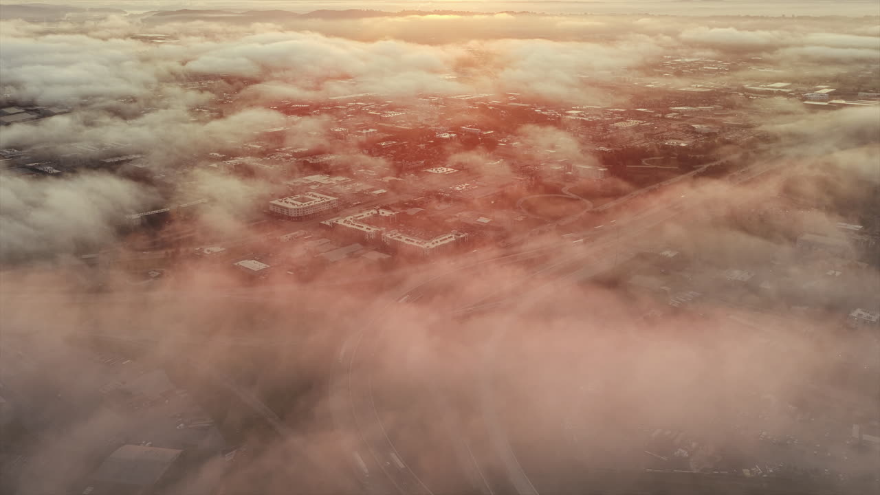 Une vue de Chattanooga prise par un drone au lever du soleil capture la ville à travers le brouillard, la ville étant faiblement visible tandis qu’une lumière dorée se répand sur le paysage brumeux.