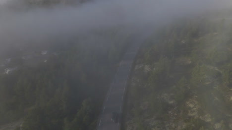 car driving on mountain road through misty forest in jotunheimen national park, norway. - aerial