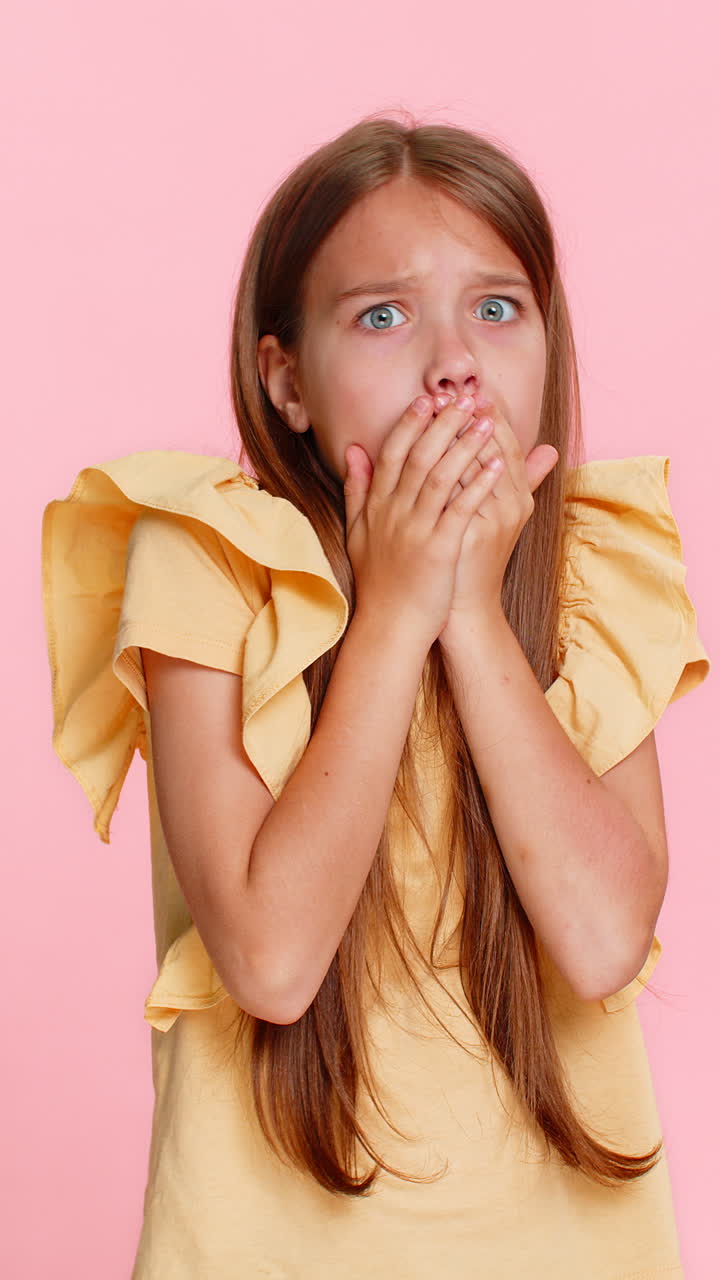 Child girl kid vividly portrays fear emotion covering mouth with hands eyes wide open shocked face