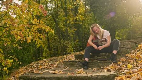 Glückliche-Junge-Songwriterin-Spielt-Gitarre-Im-Goldenen-Sonnenlicht-Des-Herbstes