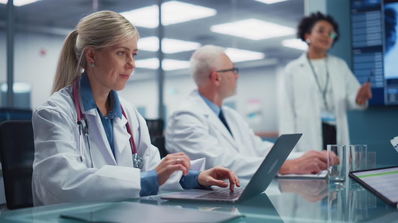 Hospital Conference Meeting Room: Female Physician Works on Laptop Computer Listens to Doctor Presenting Drug Development Data. Team of Medical Research Doctors Discuss Treatment, Medicine, Patients