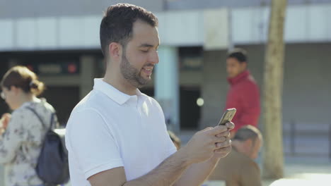 vista lateral de un hombre barbudo sonriente enviando mensajes de texto en el teléfono inteligente.