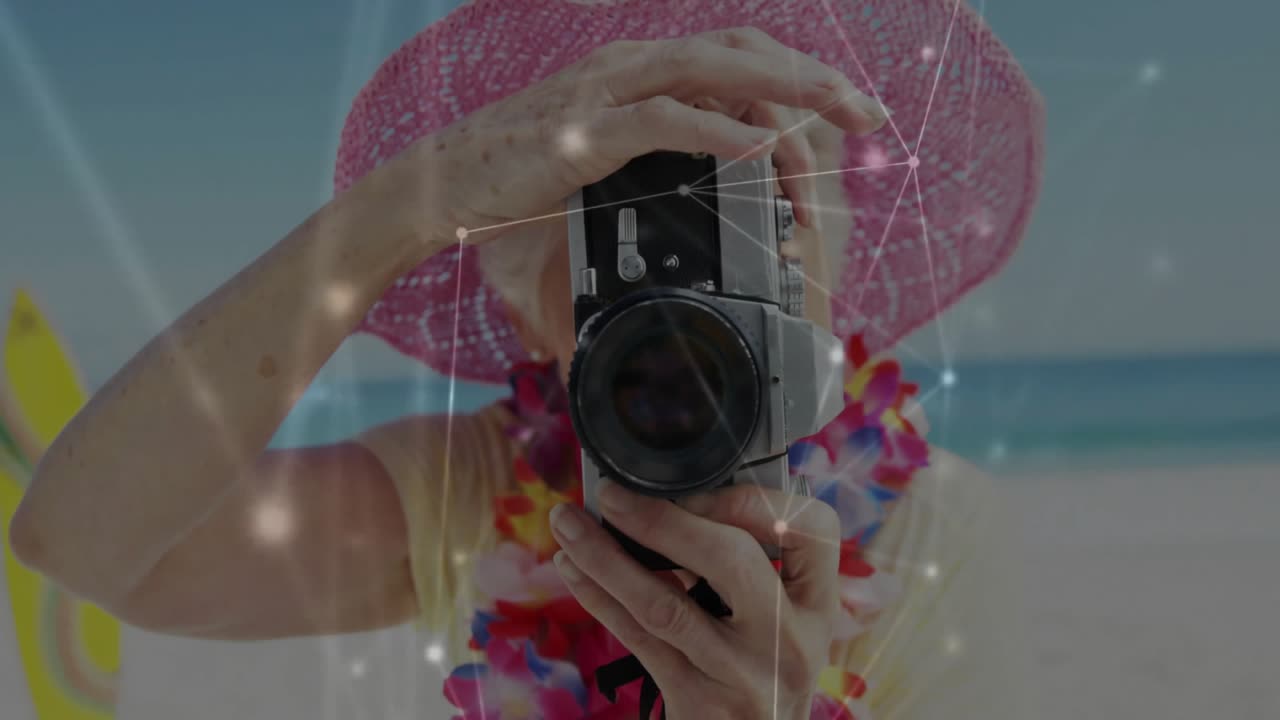 Mujer mayor levantando cámara vintage, ajustando el objetivo en la playa, mostrando una superposición de red para fotografía.