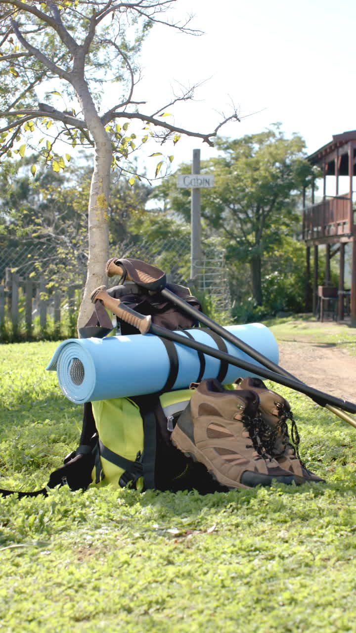 Vertical video of hiking shoes and backpack on grass at log cabin, slow motion