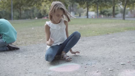 blonde girl sitting on asphalt and drawing with chalk