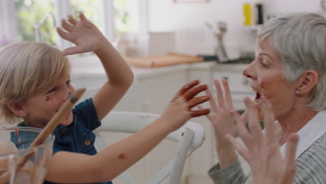 happy little boy having food fight with grandmother in kitchen covered in chocolate sauce having fun laughing playing together at home