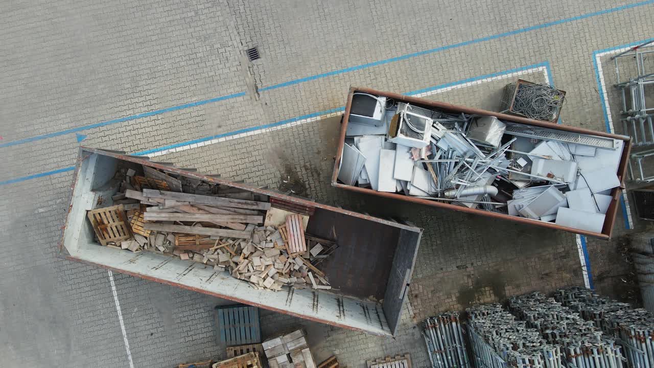 Top down aerial of Industrial containers filled with wood and metal garbage. The materials are separated for recycling. The drone slowly ascends