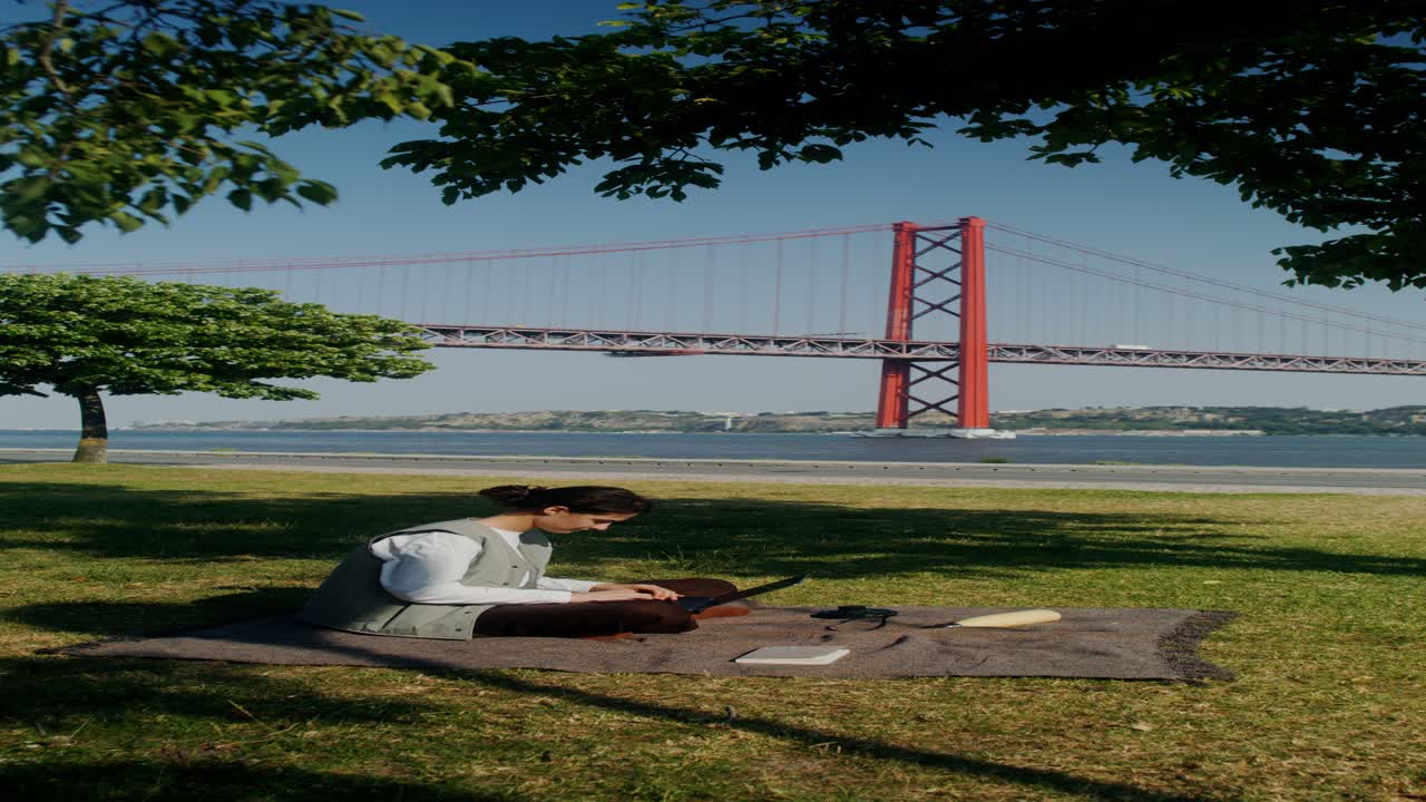 바스코 다 가마 다리 를 볼 수 있는 공원 에서 노트북 을 사용 하고 있는 여자