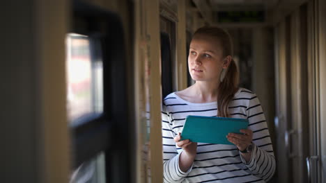 young woman with pad standing by the window in train hallway