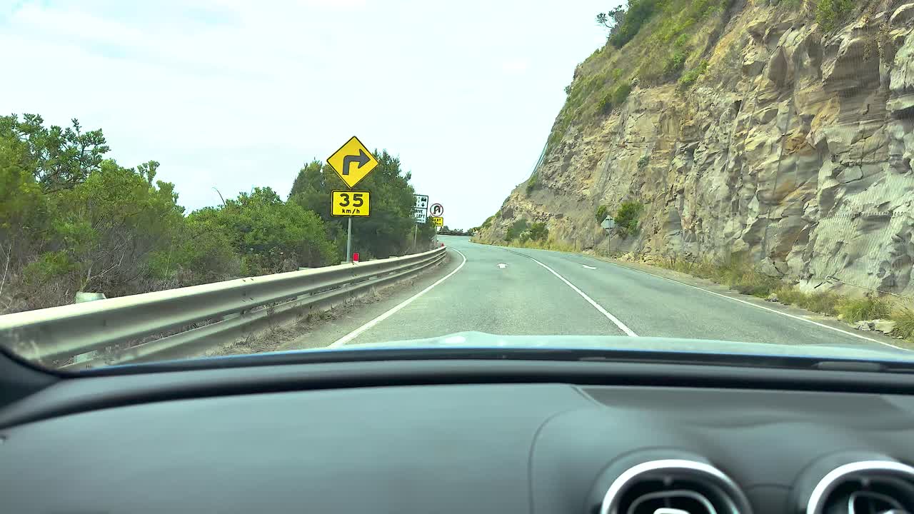 A car navigates winding roads with coastal cliffs and lush greenery under bright daylight on Great Ocean Road