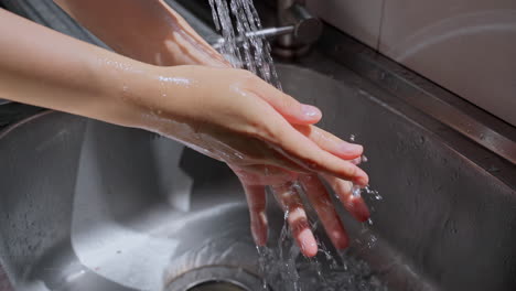 hands of woman wash their hands in a sink with soap to wash the skin and water flows through the hands