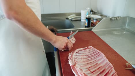 butcher trimming fat of raw lamb meat on table