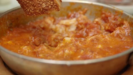 dipping sesame bread into traditional turkish menemen