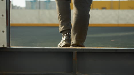 leg view of person stepping into sports arena with urban background, wearing athletic shoes on tiled pavement under soft natural light