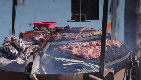 close up shot of chinchulines and various cuts of meat sizzling on a traditional argentinian asado. smoke rises from the hot coals as the barbecue cooks outdoors. a true feast.
